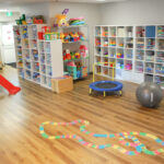 Playroom with slide, car tracks, trampoline, exercise ball and shelves of toys and games