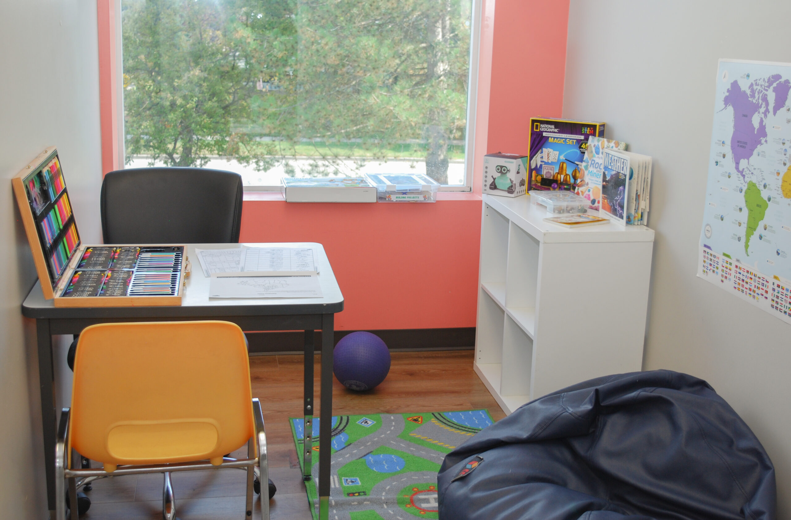 Advanced learner room set up for one to one ABA session with a table, chair, beanbag, art kit, and shelf of games and toys