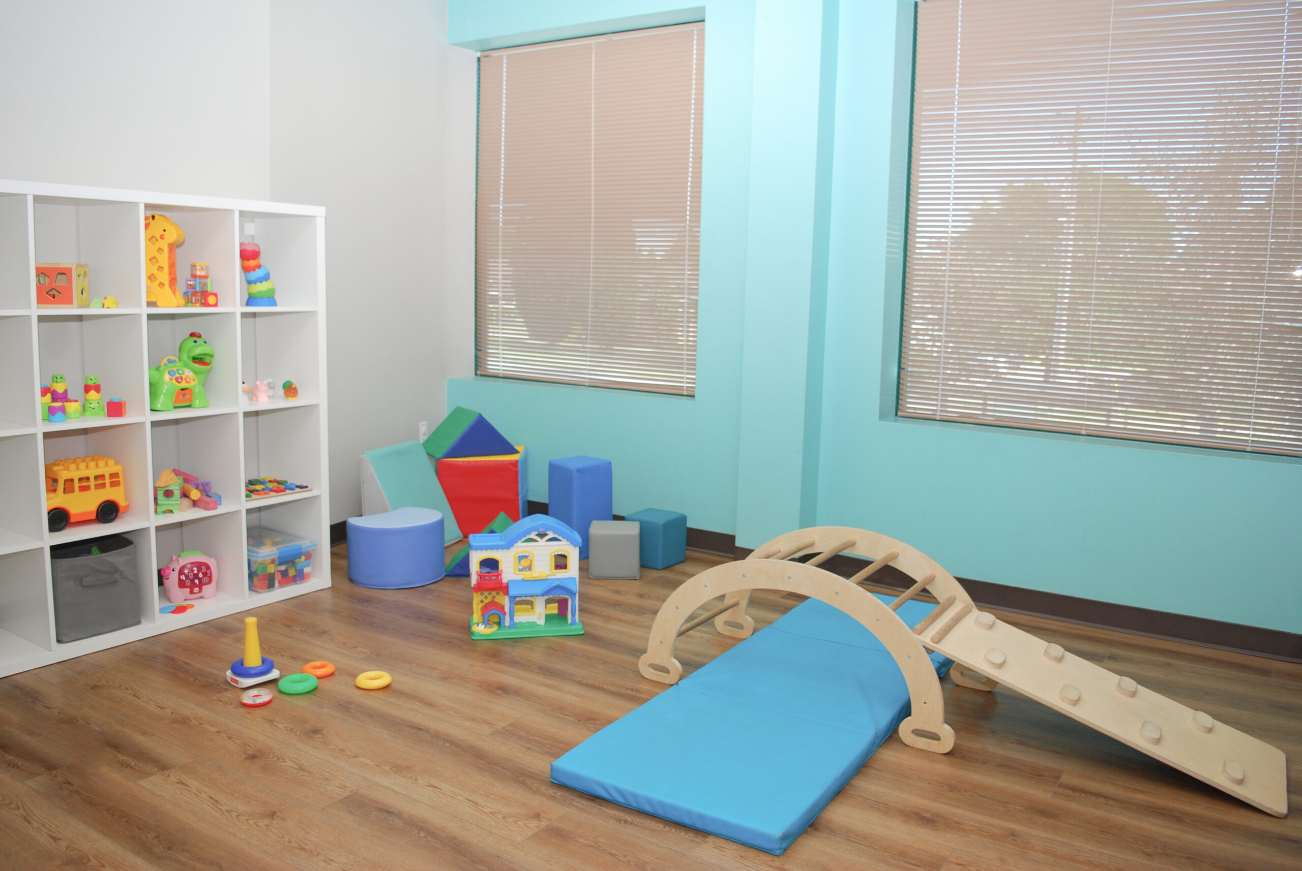 Room setup for an early learner one to one ABA session with a climber, crash mat, foam blocks, play house and shelf of toys